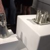 Two works of pewter on display at an art gallery. One of a little girl and the other a collection of various cups.